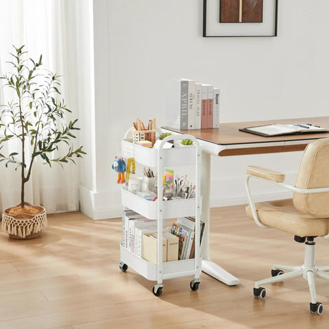 White 3-Tier Rolling Utility Cart With Caster Wheels For Kitchen And Bath next to desk, holds books and stationery.