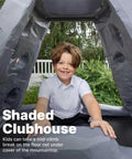 Child sitting in shaded club area of Skyward Summit Climbing Wall Playset For Kids Ages Four To Eight, 6.5 Ft Four Sided Rock Wall
