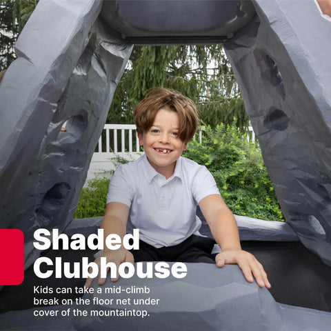 Child sitting in shaded club area of Skyward Summit Climbing Wall Playset For Kids Ages Four To Eight, 6.5 Ft Four Sided Rock Wall