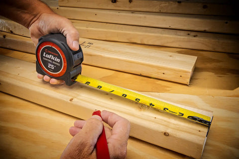 Carpenter using one and three sixteenths inch by sixteen foot tape measure with yellow clad command control anti pinch tip, measuring wood