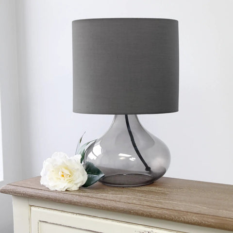 Small Glass Raindrop Bedside Table Lamp With Clear Glass Base And White Fabric Shade Easy Rotary Switch Open Bottom Base Uses 40W Bulb Cozy Nightstand Vibe Lighting For Bedroom Or Living Room on a wooden table with flower decoration.