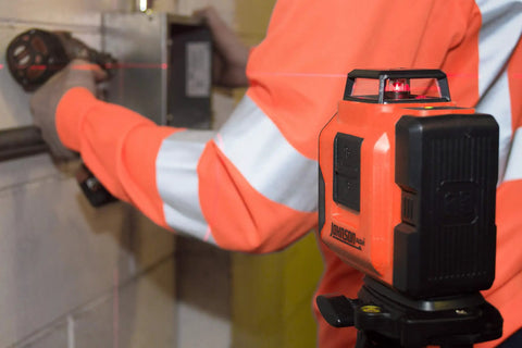 Self Leveling 360 Degree Line Laser With Horizontal And Vertical Beams 50 Ft Range on a jobsite, worker using drill in background
