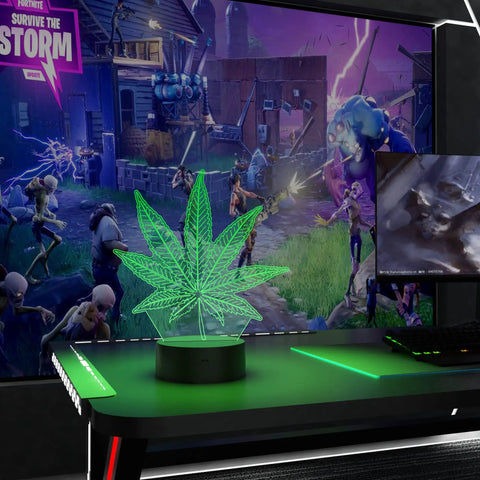 3D Illusion Night Light With Remote, 16 Color Changing LED Lamp in marijuana leaf shape on gaming desk.