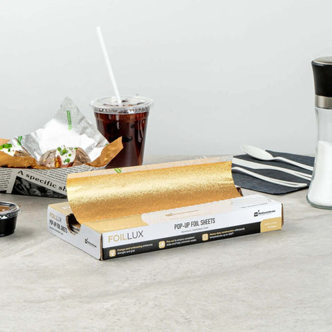 Gold Embossed Pop-Up Foil Sheets 10.8 X 9 Inch box with foil sheet partially pulled out, placed on a table with fast food items.