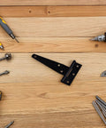 Black T shape gate hinge on wood with tools, featuring the 8 Pack Black T Shape Gate Hinges With Screws Zinc Plated T Strap Hinges.