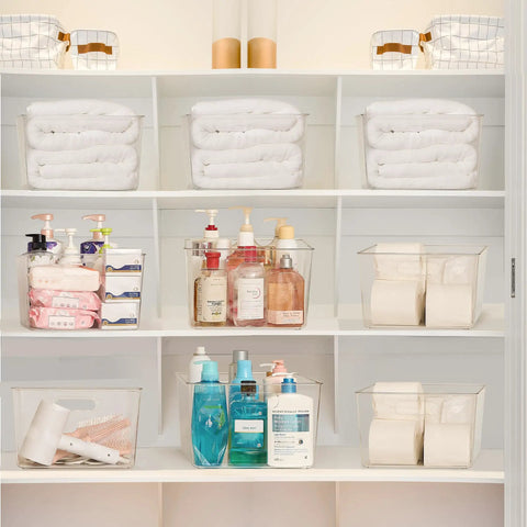 Extra Large Clear Plastic Storage Bins 4 Pack 11x11 Cube Organizer Squares With Handles For Pantry Closet Kitchen Bathroom Under Sink And Laundry Room See Through Durable Stackable Storage Containers For Clutter Busting Organization displayed in a white shelving unit holding toiletries and linens.