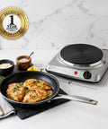 Electric Countertop Single Burner Cooktop 1000W With 7.25 Inch Cast Iron Plate beside a pan with cooked chicken on a counter.