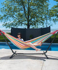 Double Cotton Hammock With Space Saving Steel Stand And Upgraded Polyester End Strings 450 Lb Capacity Premium Carry Bag Included Made From USA Grown Cotton Spacious 63 By 94 Inch Bed For Two Easy Setup And Portable Salsa Color in use by a woman by the pool.