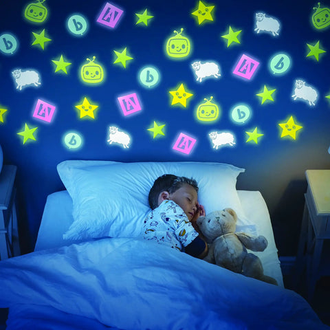 Glowing wall with Glow In The Dark Kids Sticker Pack featuring stars, sheep, and robot shapes above a sleeping child.