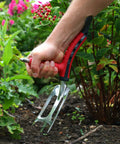 Person using Dual Grip Garden Hand Fork Cultivator And Weeder with ergonomic handles for easy digging in garden bed.