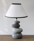 Shades Of Gray Ceramic Stacked Stone Table Lamp With Fabric Shade, 14.7 Inch Modern Bedside Light on wooden surface.