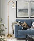 70 Inch Tall Arc Floor Lamp With Teardrop Seeded Glass Shade In Brass Finish next to blue sofa in modern living room.