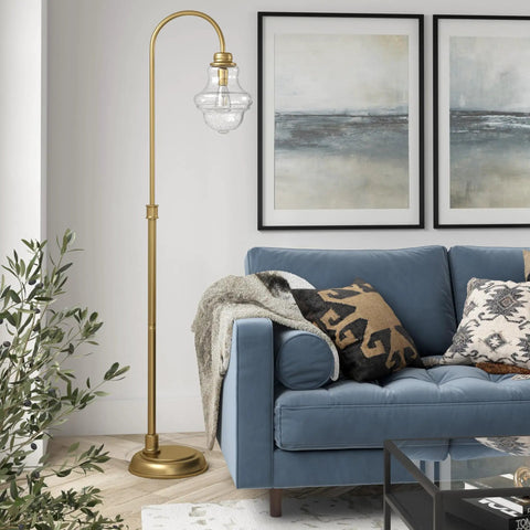 70 Inch Tall Arc Floor Lamp With Teardrop Seeded Glass Shade In Brass Finish next to blue sofa in modern living room.