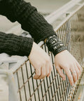 Badass Six Piece Braided Leather Bracelet Set For Men And Women Adjustable Hemp Rope Wristbands With Classic Skull Charm Punk Rock Style on a hand resting on a fence.