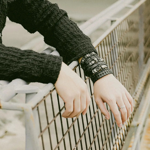 Badass Six Piece Braided Leather Bracelet Set For Men And Women Adjustable Hemp Rope Wristbands With Classic Skull Charm Punk Rock Style on a hand resting on a fence.