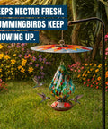 Top Shelf Bird Feeder Baffle And Rain Guard Dome Cover, Ironclad Weatherproof Shield To Keep Squirrels Out And Seed Dry, No Hassle Steel Mount Kit In Bold Red Floral Design hanging above colorful garden.