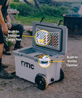 Open RTIC Ultra Light Wheeled Cooler showing features like built-in silicone cargo net and bottle opener, used outdoors