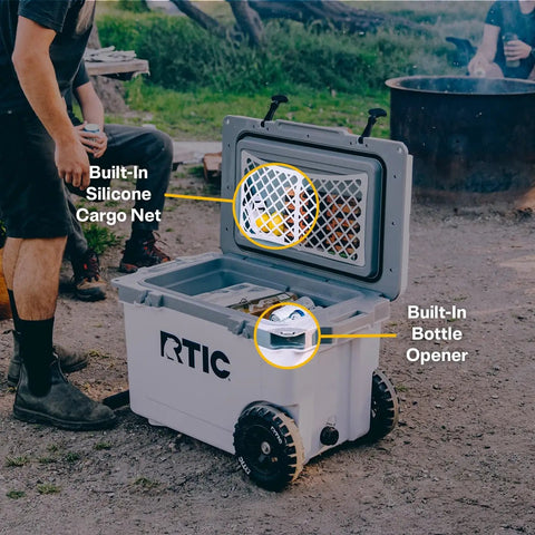 Open RTIC Ultra Light Wheeled Cooler showing features like built-in silicone cargo net and bottle opener, used outdoors