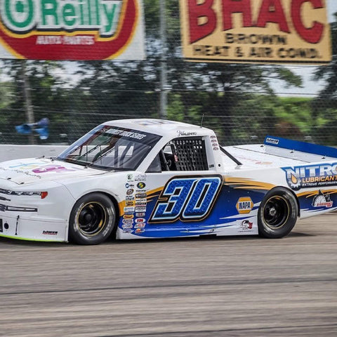 Race truck with Nitro Lubricants branding and number 30 on a track with sponsor banners in background