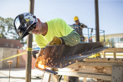 Welder using Wham 3030AE Arc Sensor Welding Mask with Pivot Headgear under bright sunlight, sparks flying from metal work.