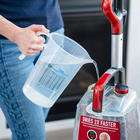Person pouring water from 64oz Half Gallon Measure Pitcher With Conversion Chart Heavy Duty Food Grade Polypropylene BPA Free Stain Resistant Translucent For Easy View Of Contents Dishwasher Safe Microwave Safe Great For Lawn Pool Spa Agriculture Home Hobbies Lye Cooking into a steam cleaner.
