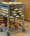Rolling stainless bakery rack with croissants on multiple tray shelves and four caster wheels