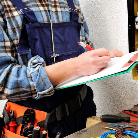 Mechanic in blue overalls writing on clipboard with tools in belt