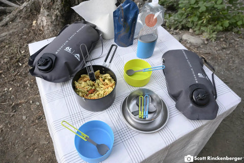 Two Person Camping Cook Set With Nesting Design Deep Dish Bowls And Double Wall Insulated Mugs Lightweight Two Liter Hard Anodized Pot Nonstick PFOA Free Safe For Hot Or Cold Meals Ideal For Backpacking Or Family Camps on a table with pasta and camping accessories