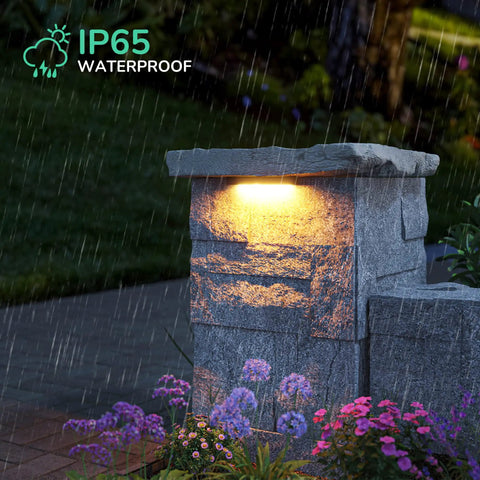 Outdoor LED hardscape light on stone pillar illuminating garden, IP65 waterproof, part of 8 Pack Outdoor LED Hardscape Lights For Steps Retaining Walls And Decks, 7 Inch Paver Lights, 12V ACDC 2W 2700K Low Voltage, IP65 Waterproof, Wide Voltage Range, Easy Install Landscape Lighting.