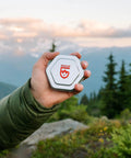Person holding compact Aquaseal FD River and Sea Repair Kit with Four Tenacious Tape Hex Patches, scenic mountain view in background