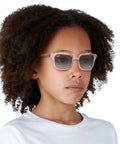 Child wearing RJ9071S Kids Square Sunglasses for Narrow Faces, Transparent Pink Frame With Light Gray Gradient Lenses, 48 mm