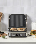 Cuisinart Griddler FIVE Electric Grill With Panini Press grilling chicken breasts on nonstick plates, LCD timer, and stainless steel base.