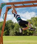 Child playing on Skyfort II Cedar Wood Swing Set With Wave Slide, Raised Clubhouse, monkey bars, outdoor backyard playset.