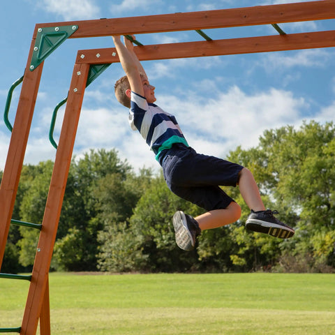 Child playing on Skyfort II Cedar Wood Swing Set With Wave Slide, Raised Clubhouse, monkey bars, outdoor backyard playset.