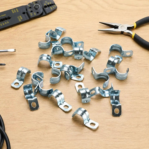 Heavy Duty One Hole 1/2 Emt Straps 100 Pack Zinc Plated Steel Conduit Clamps for Electrical Tubing scattered on wood surface.