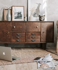 Mid-century wooden sideboard in a cozy living room with wicker chair and wall art.
