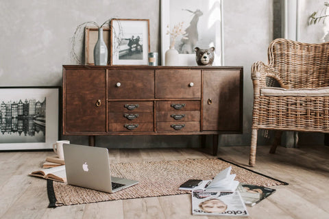 Mid-century wooden sideboard in a cozy living room with wicker chair and wall art.