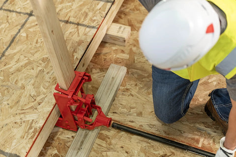 Guardian 2601 portable wall jack, red cast-iron clamp securing a wooden post on a construction site.