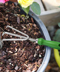Three Tine Claw Garden Rake With Ergonomic Handle And Stainless Steel Build in use loosening soil around plant