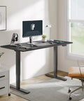 Height adjustable standing desk with a spacious 60 by 24 top, matte black frame, and dual motor lift in a bright workspace.