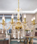 Lux Gold Tone Crystal Chandelier With 8 K9 Crystals Modern Glass Pendant Light shining in living room space.