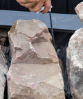 Applying Waterfall Foam Sealant For Ponds between rocks, showing black polyurethane foam filling gaps and securing stones.