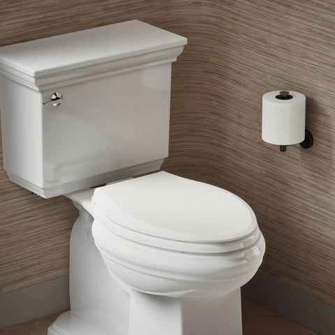 Angled front view of white ceramic elongated toilet with closed lid and chrome lever, against brown textured walls.