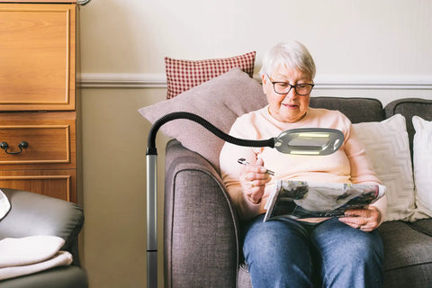 MultiFlex LED Floor Magnifier Lamp With Ultra Wide 6 Inch Viewing Area in use, silver finish, aiding reading on a couch.