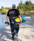 Person walking towards lake carrying Sonicwake RC Boat 48 Inch Self Righting Brushless 8S Ready To Run with controller