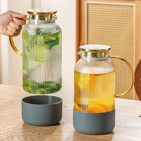 Two Piece Glass Pitcher Set Including Secure Glass Lid And Cushioned Anti Slip Silicone Base For Kitchen Counter Safe Serving Heavy Duty Water Jug Hassle Free Dispensing For Iced Coffee And Fresh Juice on wooden table, filled with lime and orange slices.