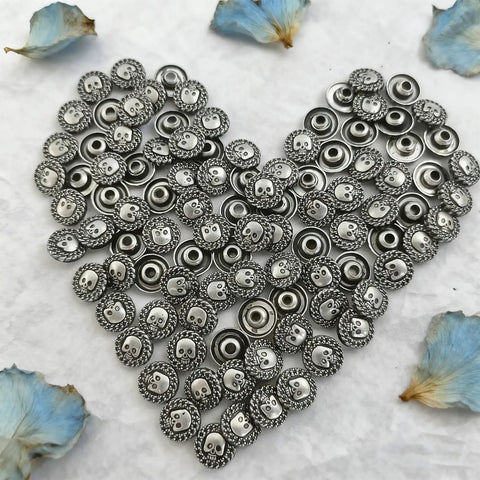 Top Shelf Badass Metal Skull Buttons And Screw Back Rivets For Leather Crafting 100 Pc Bulk Set in a heart shape arrangement.