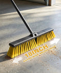 Heavy Duty 18 Inch Push Broom With Adjustable Metal Handle And Stiff Flagged Bristles on concrete floor, sweeping dirt.