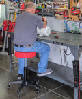 Man seated on Rolling Shop Stool With Adjustable Height For Mechanics Padded Garage Seat With Smooth Rolling Wheels in workshop.