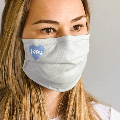 Person wearing light-colored face mask with blue heart logo.